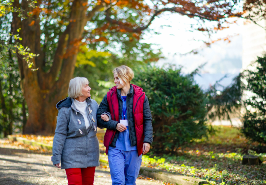 Femme âgée et aide-soignante marchant et parlant dans un parc.