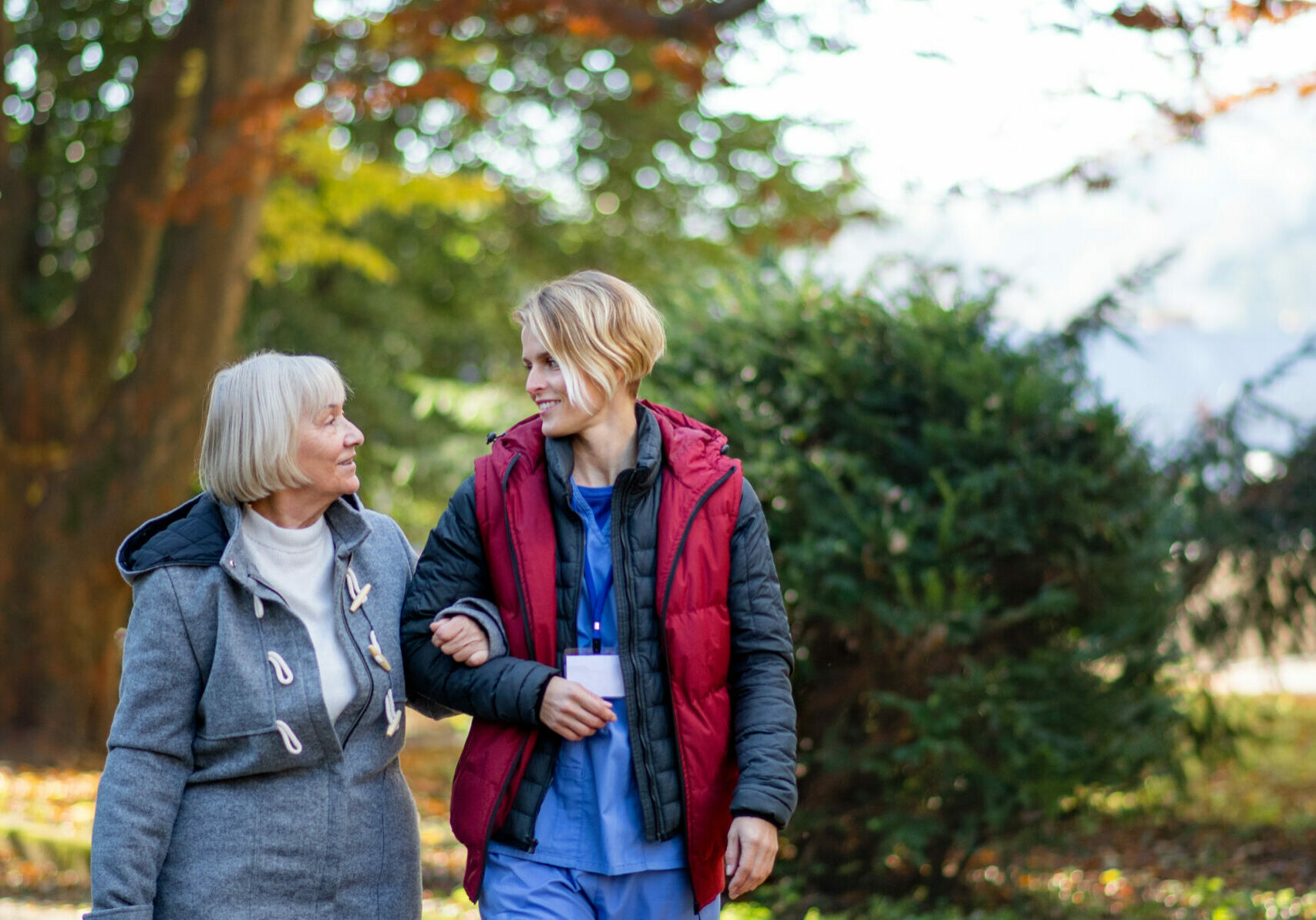 Front view of senior woman and caregiver outdoors on a walk in park, talking.